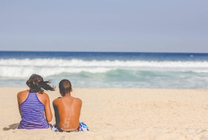 two people sitting on beach looking out at waves and horizon