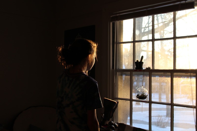 Person standing in dark room looking out window 