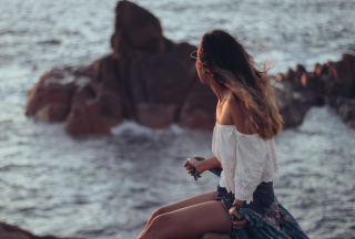longhaired-girl-sat-on-rocks-by-the-water-looking-at-horizon