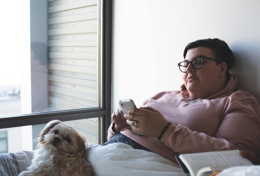 Woman on the phone in bed with her small dog