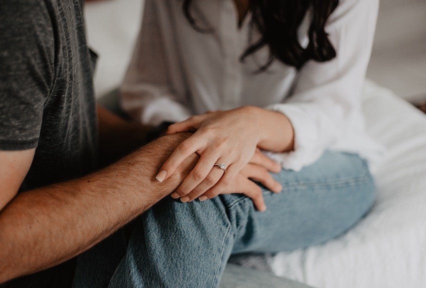 Two people sitting close together holding hands in a supportive way