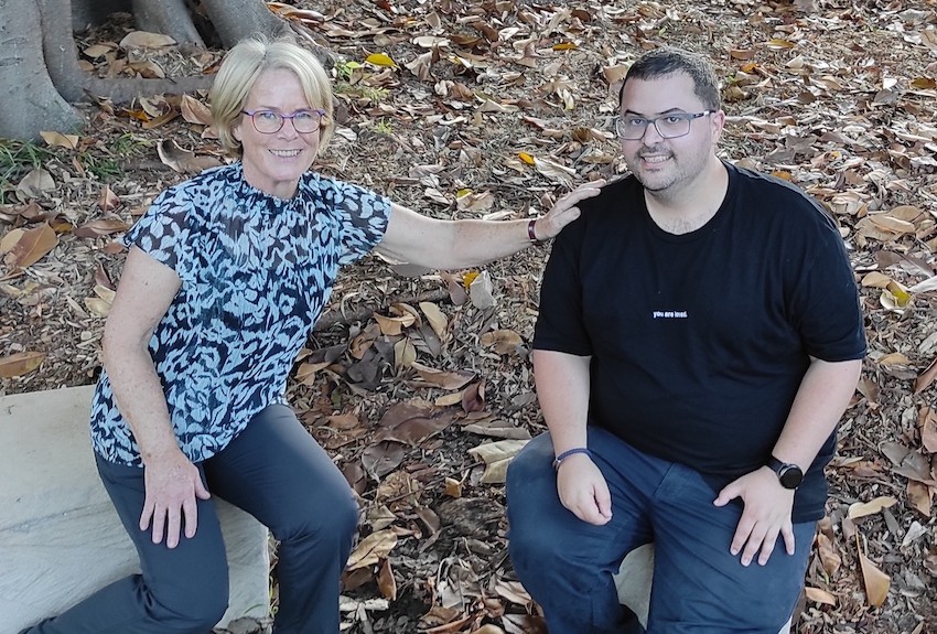 Marg and Mark sitting together outdoors smiling at the camera, Marg has her hand resting on Mark's shoulder