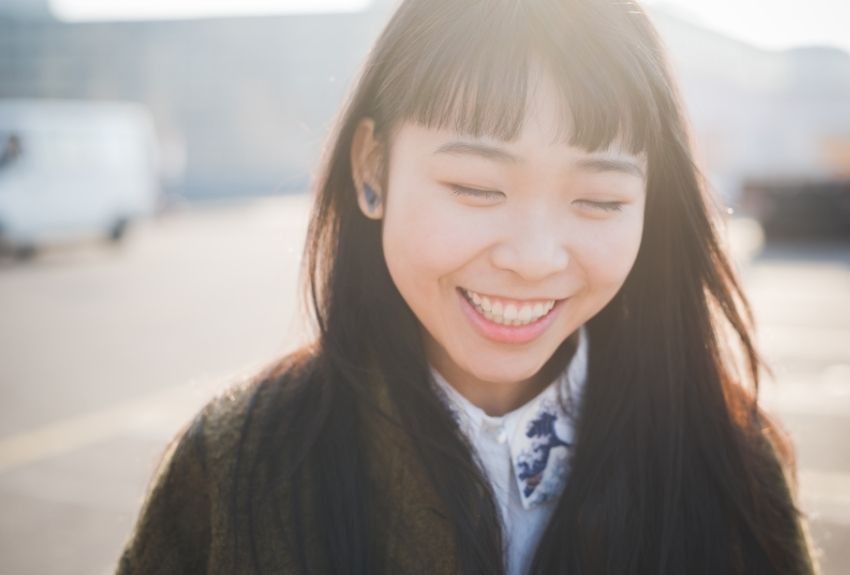 Person looking down and smiling they are outside and sun is shining on them.