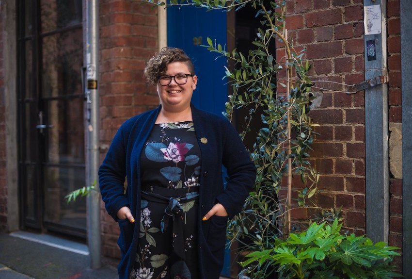 Jess stands outside smiling with hands in pockets