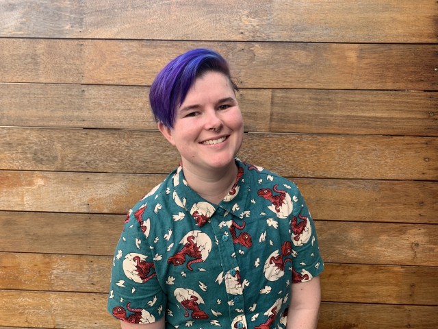 Holly smiling, wearing purple hair and a green collared shirt