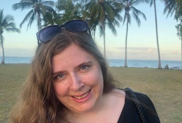 Bron on the beach with palm trees and the ocean behind her