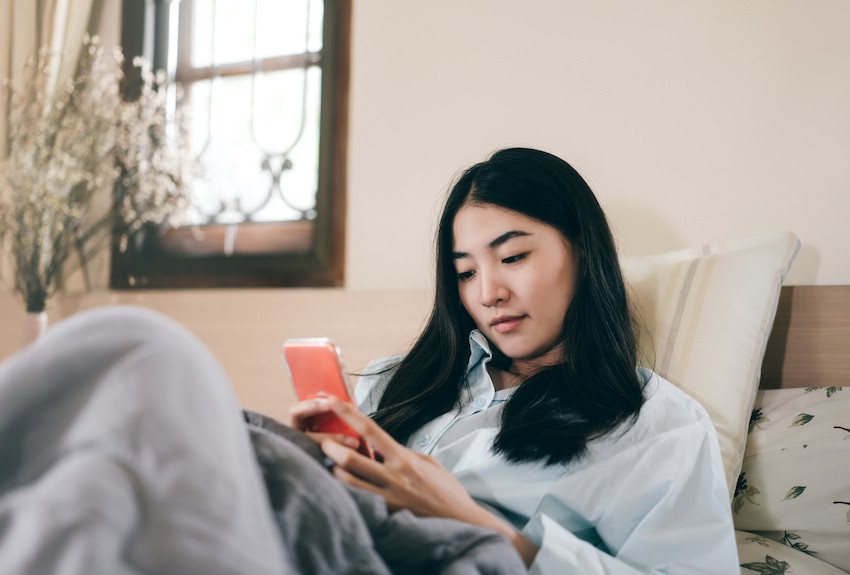 Woman lying in bed looks at her phone
