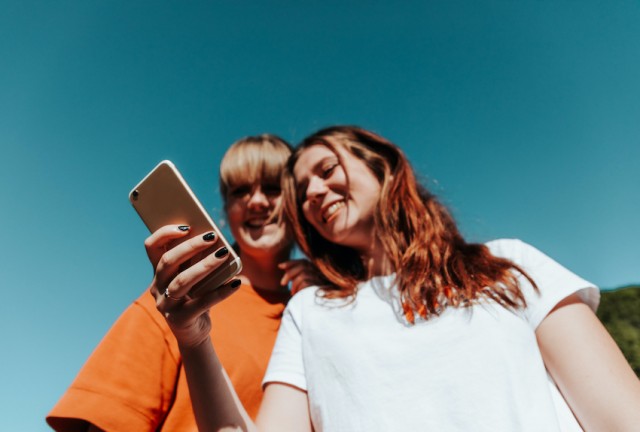 Two young people laugh and smile together reading from a phone.