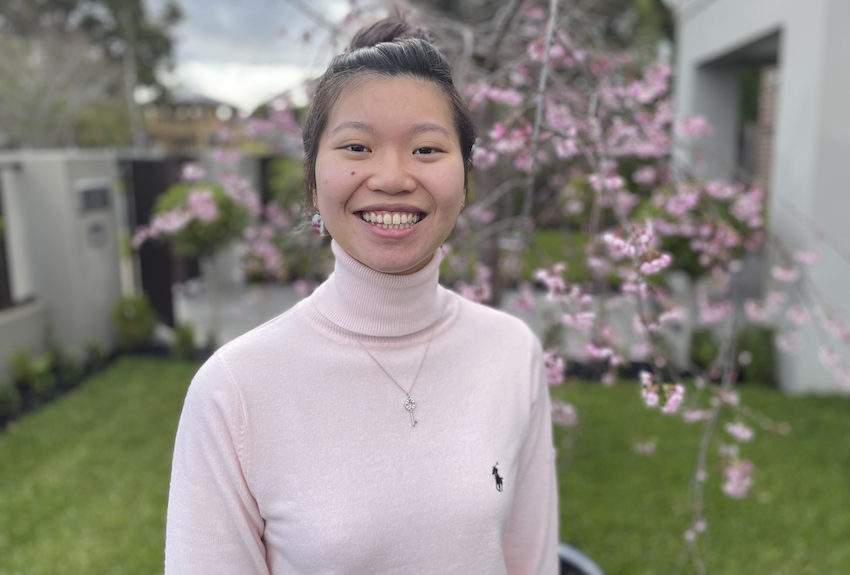 Image of SANE Peer Ambassador Jeanette Chan. Jeanette is a young woman in her twenties with south-east Asian appearance. Her dark hair is drawn back in a bun and she is smiling warmly. She wears a pale pink turtleneck jumper that matches the tree blossoming in the background of the image.