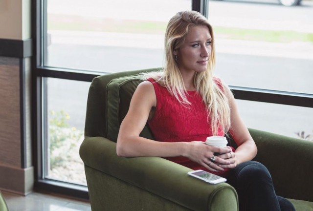 Person is sitting in a comfortable chair with a coffee and looking out the window thoughtfully.