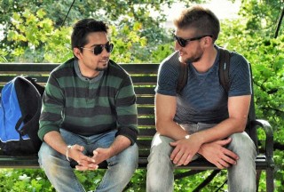Two men sit on a bench outside having a chat