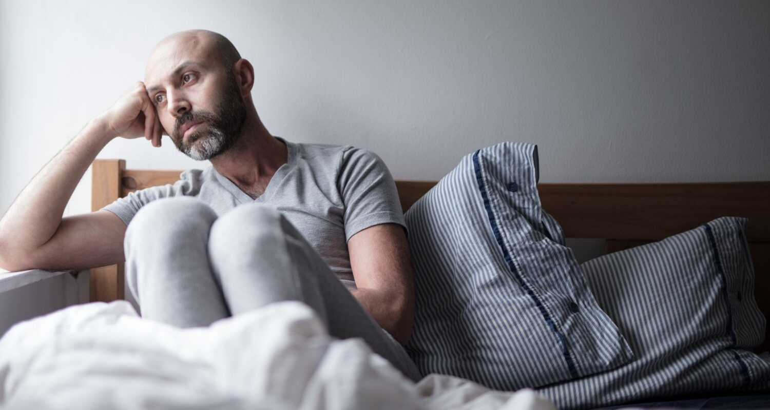 Man sitting on bed, looking pensive