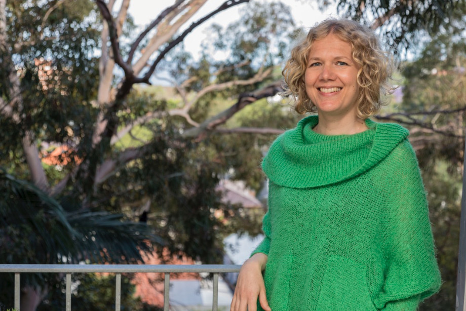 Vanessa Kredler, SANE Peer Ambassador, wearing a green top and standing on a balcony with trees behind her
