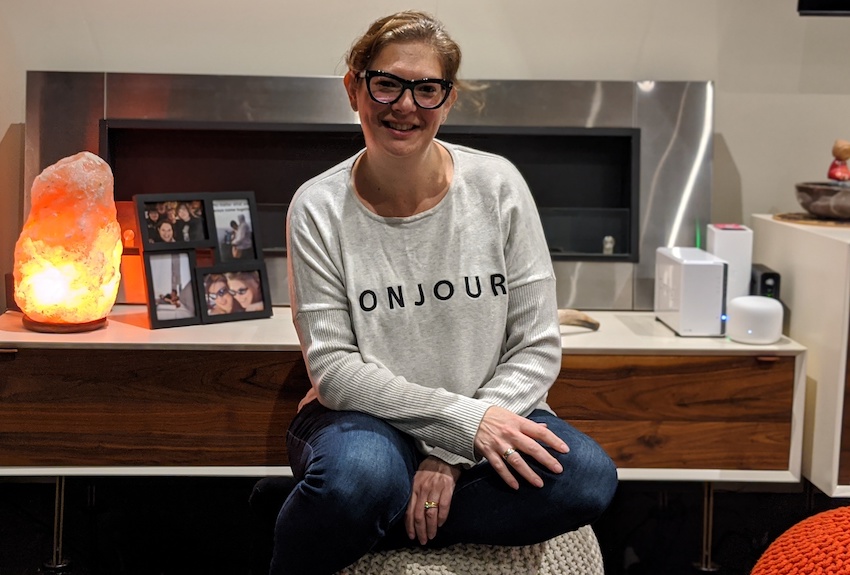 Lisa sits smiling with her arms across her lap, a salt lamp and family photos in the background