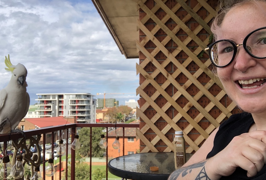 Sophie sitting outside on a balcony, smiling as a cockatoo sits on the rail nearby