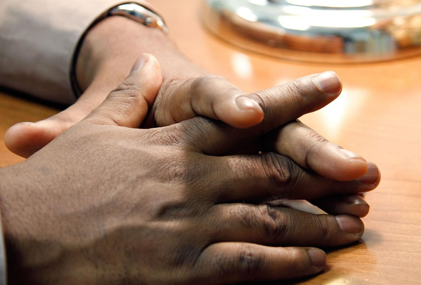 Hands resting on table with fingers interlocking.