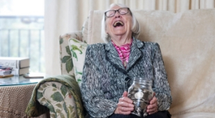Elderly woman with money jar laughing