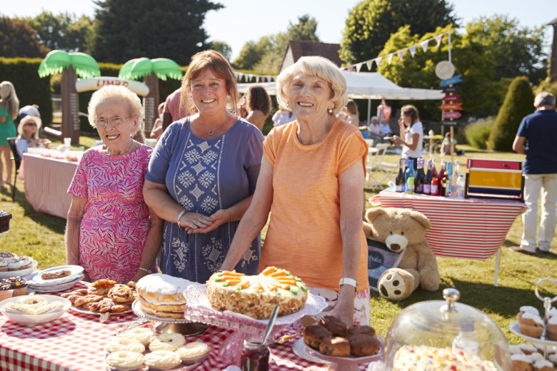3 older women running a cake stall on a sunny day