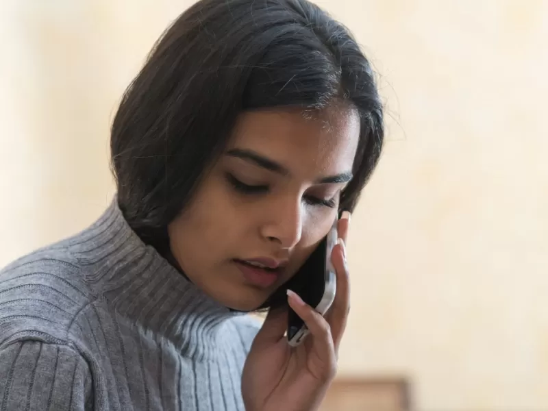 Young woman with rhost black hair wearing a grey turtleneck sweater while talking on a mobile phone